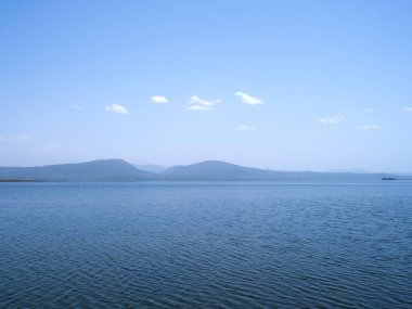 Göl ve dağlar, güzel, etkileyici göl ve dağların manzara fotoğrafı. Mavi güneşli gökyüzü, küçük bulutlar. Uzakta, elektrik enerjisi için kurulmuş yel değirmenleri tepelerde görülebilir..