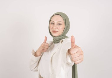 Sen harikasın. Genç beyaz kadın gülümseyen müslüman kadın portresi kameraya baş parmak işareti yapıyor. Elimizdeki seçici odaklanma. İzole edilmiş gri stüdyo arka planı. Önerilen teklif kavramı.
