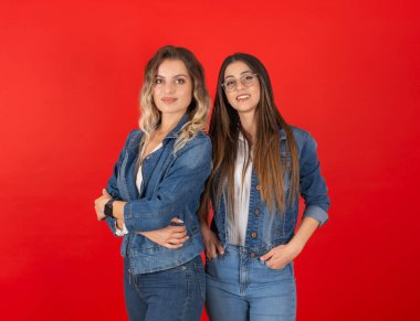 Denim stili, iki güzel 20 'li yaşlarda beyaz bir kadının portresi kırmızı stüdyo arka planında duruyor. Kot elbiseli mankenler. Formda, tapılası şık insan yaşam tarzı..