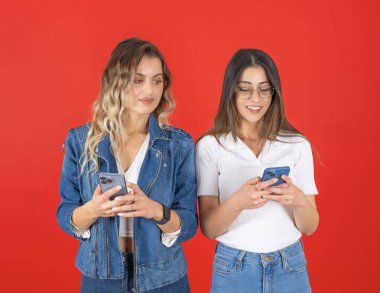 Akıllı telefonları gözetlemek, en iyi arkadaşının akıllı telefonuna gizlice bakan beyaz bir kadının görüntüsü. İzole kırmızı arka plan. İlginç bir arkadaşlık ve dedikodu fikri fotoğrafı..