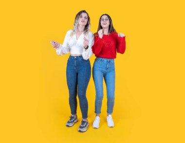 Enerjik genç iki kız dans ediyor, tüm vücudu beyaz 20 'li yaşlarda enerjik genç iki kız stüdyo sarısı arka planda el sallıyor. Gülümseyen mutlu iki kadın müzik dinler..