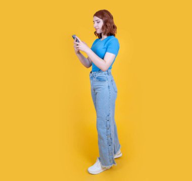 Akıllı telefon kullanarak, 20 'li yaşlarda, genç, beyaz saçlı, akıllı telefon kullanan bir kadın. Ekrana bak, daktilo mesajı tut, çevrimiçi alışveriş yap, sarı arkaplan üzerinde trend uygulaması kullan.