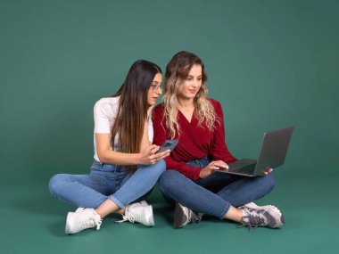 Uzaktan kumandalı, tam vücut görüşlü, iki beyaz kadın aynı katta oturuyor dizüstü bilgisayar ve akıllı telefon kullanıyor ve uzaktan kumandalı ekranı çalıştırıyor. E-öğrenim konsepti fikir imajı.