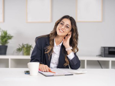 Oldukça güzel bir iş kadını, güzel bir iş kadınının beyaz portresi ofis masasında oturmuş kahve içerken notlar yazıyor. Kameraya gülümsüyor. Resmi gömlek ve ceket giy..