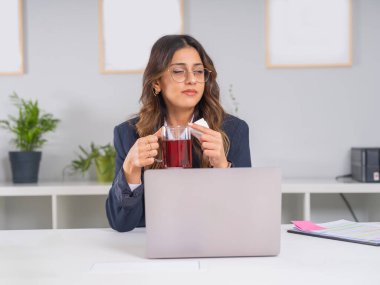 İş kadını soğuk algınlığına yakalandı, 20 'li yaşlarda beyaz esmer bir iş kadınının portresi ofiste mendile hapşırırken yakalandı elinde dizüstü bilgisayarında kış çayı tutarken. Sağlık, alerji, hastalık konsepti.