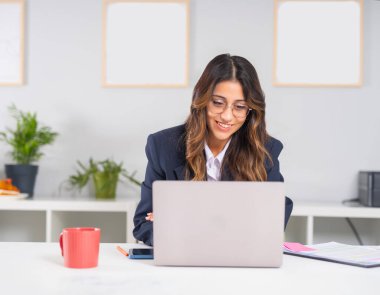 Dizüstü bilgisayar kullanan iş kadını, ofisteki dizüstü bilgisayarını kullanarak gülümseyen mutlu beyaz kadın portresi. Şık esmer bayan yönetici takım elbise giyme projesi.