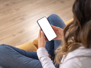 Cep telefonu modeli, uzun saçlı, esmer, genç bir kadının evde oturan koltuğunun üstünden beyaz dokunmatik ekranlı cep telefonu taklidi. Uygulama reklam kavramı.
