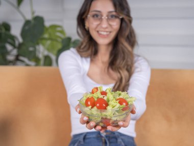 Sağlıklı taze salata, sağlıklı taze salata yiyen neşeli beyaz kadın. Salata, domates ve vejetaryen yemeklerle dolu cam kaseye odaklan. Evde otururken, boşluğu kopyala.
