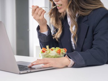 İş kadını salata yiyor, kafkasyalı esmer bir iş kadınının ofis masasında salata yerken resmi takım elbise giymesini yakından görüyor. Sağlıklı yaşam tarzı kavramı.