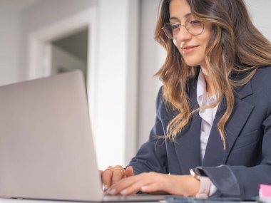 Dizüstü bilgisayar kullanarak gülümseyen iş kadını, 20 'li yaşlarda, kendine güvenen esmer, gülümseyen iş kadınının dizüstü bilgisayarı kullanan yakın görüntüsü. Kendine güvenen kadın ofis çalışanı sonuçlardan memnun.