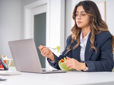 Hüsrana uğramış mutsuz iş kadını istemeden salata yiyor, beyaz tenli sağlıklı görünümlü esmer ofis çalışanı salata yemek istemiyor gibi görünüyor. Dizüstü bilgisayar konsepti kullanılıyor.