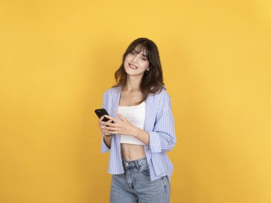 Genç, mutlu, neşeli, beyaz, 20 'li yaşlarda, esmer, beyaz tişörtlü, sıradan giyinen, el ele kameralı, sarı arka planda izole edilmiş, cep telefonuyla sohbet eden bir kadın..