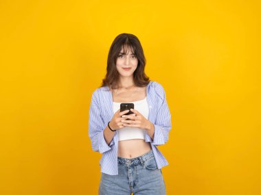 20 'li yaşlarda beyaz seksi bir kadının cep telefonuyla mesajlaşırken, kameraya bakarken, gülümserken, sarı arka planda beyaz bluz giyerken, boşluğu kopyalarken fotoğrafı..