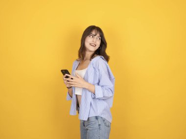 Cep telefonu kullanan, gülümseyen, arka planda izole bir şekilde duran, fotokopi alanı çalışma alanına gülümseyen bir kadının yan görünüm portresi. Beyaz bluz, gömlek ve kot pantolon giy..