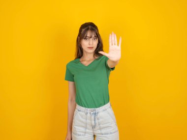 Dur dedim! Bir elini uzatan 20 'li yaşlarda beyaz, esmer bir kadının portresi. Kameraya avucunu aç. Tabu işaretini durdur, reddet, konsept fikir imajını azalt. Sarı arkaplanda duruyor, boşluğu kopyala.