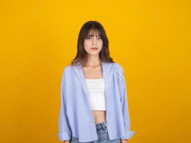 Ciddi bir genç kadın kamerası, beyaz yirmili yaşlarda esmer bir kadının portresi. Stüdyonun sarı arka planında izole edilmiş kameraya bakan ciddi bir genç kadın. Beyaz bluz giyiyor. İnsanlar yaşam tarzı duyguları.