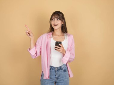 Çevrimiçi alışveriş konsepti, heyecanlı genç beyaz 20 'li yaşlarda kadın cep telefonu kullanıyor. Cep telefonu görünümlü fotokopi alanı kullanıyor. Promosyon metni alanını mobil uygulama kullanarak gösteren bej stüdyo arka planında izole edilmiş..