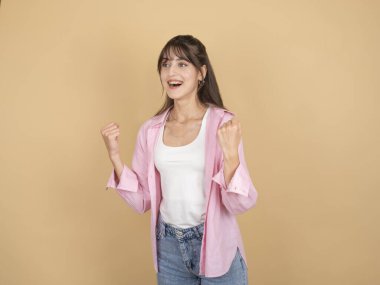 Kazanan jest yapan bir kadın, 20 'li yaşlarda beyaz bir gencin komik, neşeli, mutlu bir kadının basit pembe gömleğiyle jest yapıp yumruklarını sıkmasını gösteren bir fotoğraf. Evet de, zafer bej arka planda.