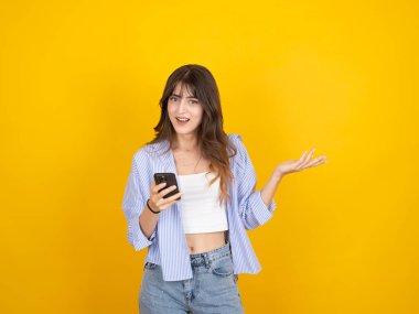 Telefon kullanan mutlu bir kadın, 20 'li yaşlarda, gülümseyen mutlu bir kadın telefon kullanıyor sarı arka plan stüdyo resmine izole edilmiş eller yayıyor, fotokopi odası. Şaşırtıcı yüz hareketi..