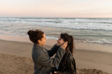 Smiling woman giving earphone to friend on beach in evening  clipart