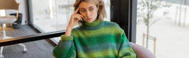 thoughtful young woman in green sweater sitting in lobby of hotel in Barcelona, banner  clipart