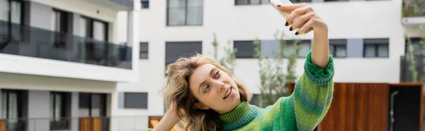 stock image happy woman in sweater taking selfie on smartphone near hotel in Barcelona, banner 