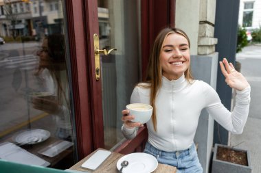 Viyana 'da bir kafede el sallarken kaygısız bir kadın elinde bir bardak kapuçino tutuyor. 