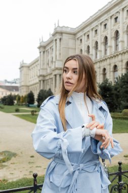 Viyana 'da tarihi binanın yakınında beklerken mavi trençkotlu genç kadın kol saatini kontrol ediyor. 
