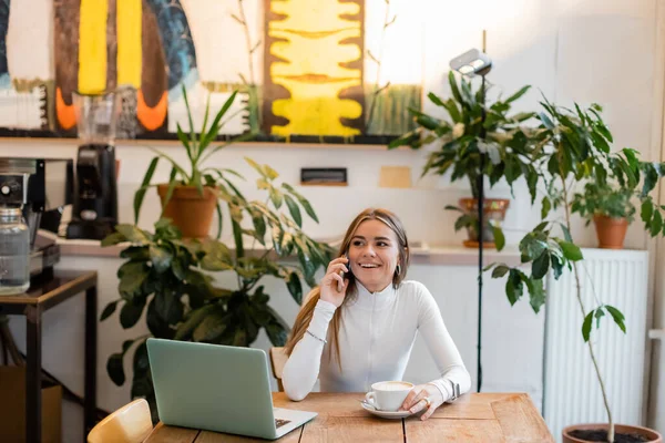 Bilgisayarın Yanındaki Kafede Kapuçino Bardağının Yanında Akıllı Telefondan Konuşan Mutlu — Stok fotoğraf