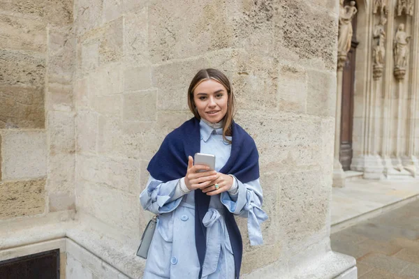 Ung Kvinna Med Marinblå Halsduk Ovanpå Trenchcoat Håller Mobiltelefon Nära — Stockfoto