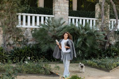 Sıcak ceketli ve kulaklıklı neşeli ve serbest çalışan. İspanya 'nın Barcelona şehrinde gündüz vakti parkta köpekleri gezdirirken kameraya bakıyor ve cihazları tutuyor. 