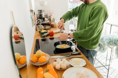 Cropped view of bearded man seasoning fried eggs with peppercorns from mill  clipart