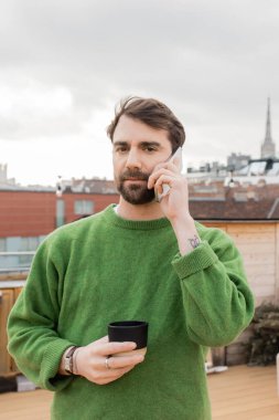Atlayan adam Viyana, Avusturya 'da elinde bir fincan kahveyle akıllı telefondan konuşuyor.