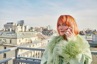 Akıllı telefondan konuşan ve Viyana, Avusturya 'da çatı terasında kameraya bakan trend bir kadın.