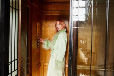 trendy woman looking at camera from vintage elevator in residence building in Vienna, Austria clipart