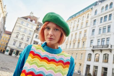 Modern sokak modası, bereli ve parlak yelekli moda kadın Viyana 'da caddede kameraya bakıyor.
