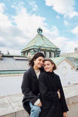 Mutlu lezbiyen çift bir kubbenin önünde gülümsüyor ve sarılıyorlar, Viyana 'da huzurlu bir an.