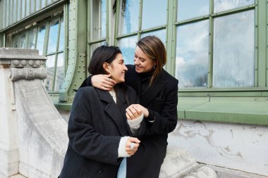 happy lesbian woman embracing her girlfriend near Palmenhaus in Vienna on background, Austria clipart