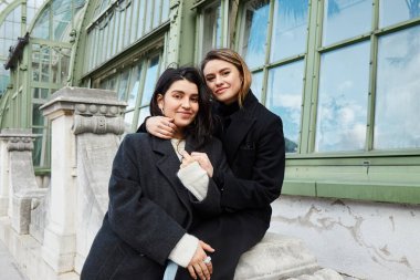 Siyah ceketli mutlu lezbiyen çift Viyana 'da Palmenhaus yakınlarında kucaklaşıyorlar.