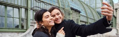 Mutlu lezbiyen çift Viyana 'da tarihi bir yerin yanında dururken selfie çekiyorlar, yatay pankart