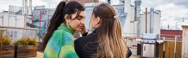 stock image banner of tender moment between young lesbian women sitting together on a rooftop, cityscape
