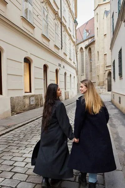 在欧洲城市 一对穿着时髦外套 手牵手散步的快乐的年轻女同性恋夫妇 免版税图库图片