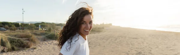 Cheerful young woman in white t-shirt smiling on sandy beach in Spain, banner — Stock Photo