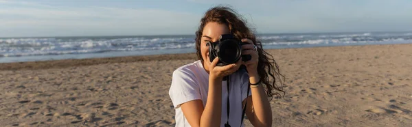 Curly woman in white t-shirt taking photo on digital camera in Spain, banner — Stock Photo