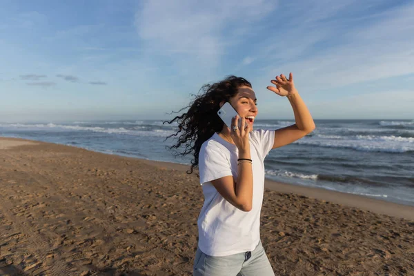 Amazed woman in white t-shirt talking on smartphone on sandy beach in Barcelona — Stock Photo