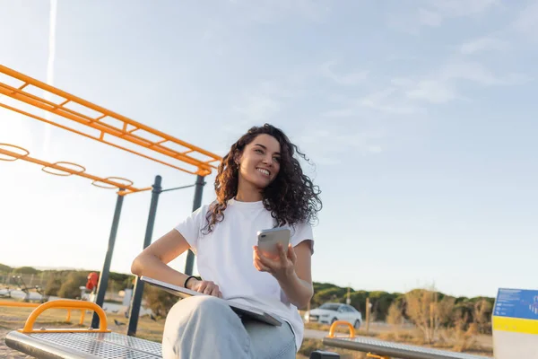 Low angle view of cheerful freelancer holding smartphone near laptop on beach in Spain — Stock Photo