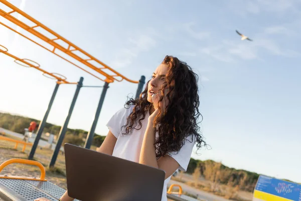 Low-Winkelansicht des lockigen Freelancer mit Laptop während er am Strand von Barcelona auf dem Smartphone spricht — Stockfoto