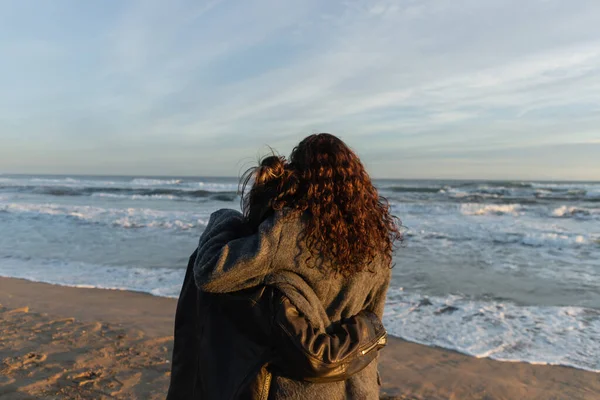 Back view of friends hugging on beach near sea in Spain — Stock Photo