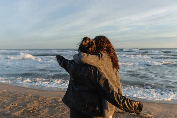 Vista trasera de la mujer abrazando amigo en la playa en Barcelona - foto de stock