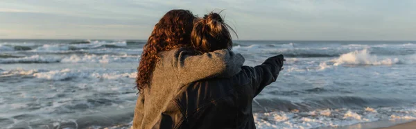 Vista trasera de la mujer abrazando amigo en la playa en Barcelona, bandera - foto de stock